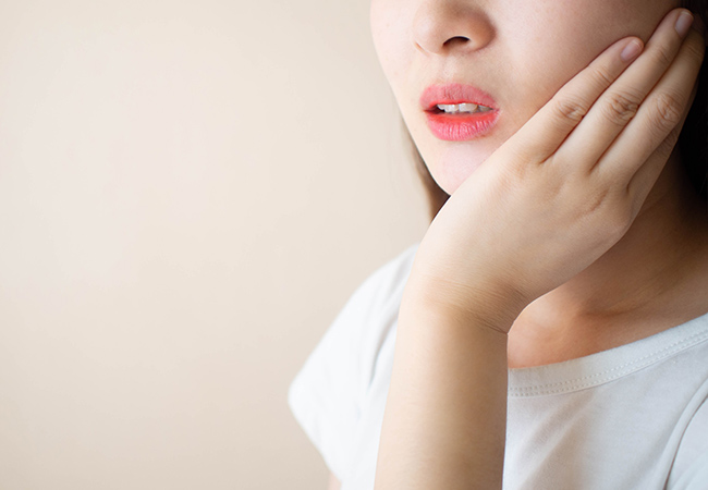 歯に痛みを感じ頬に手をあてる女性